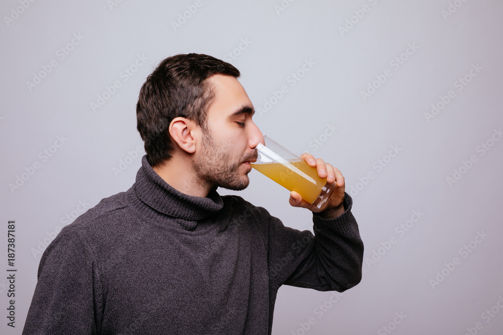 Fototapeta premium Handsome man is drinking orange juice on gray background