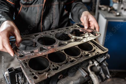 Sealing gasket in hand. The mechanic disassemble block engine vehicle. Engine on a repair stand with piston and connecting rod of automotive technology. Interior of a car repair shop. photo