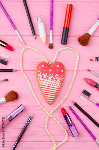 Flat lay cosmetics for Valentines Day. Heart shaped red cookie on pink wooden background. Cosmetics and accessories romantic composition.