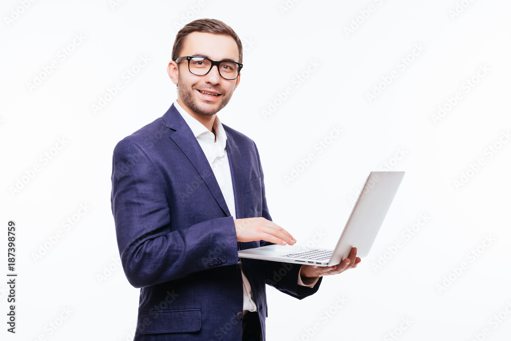 Side view of attractive young businessman in classical suit using laptop, standing against white background