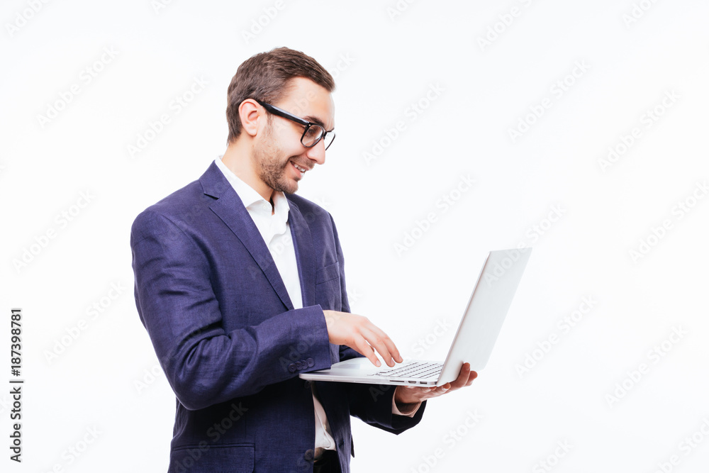 Side view of attractive young businessman in classical suit using laptop, standing against white background