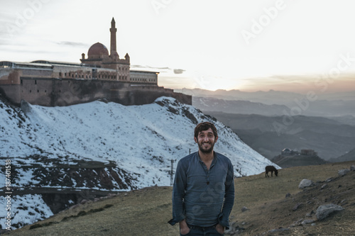 smiling kurdish man with beard in front of oriental palace at sunset in the mountains photo