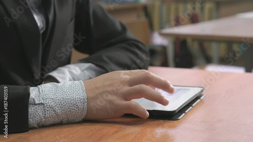 Close-up of hand of student boy dressed in black suit sits at desk at office the resting and looking at favorite photos using the screen of computer tablet in white-black colour. photo