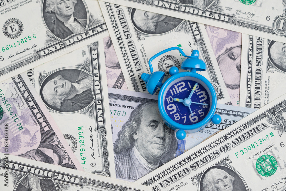 Blue retro alarm clock on US dollar banknotes as money time concept Blue retro alarm clock on US dollar banknotes as money time concept