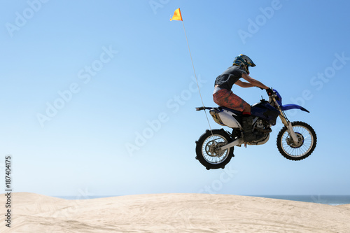 Teenager jumping sand dunes on a motorcycle photo