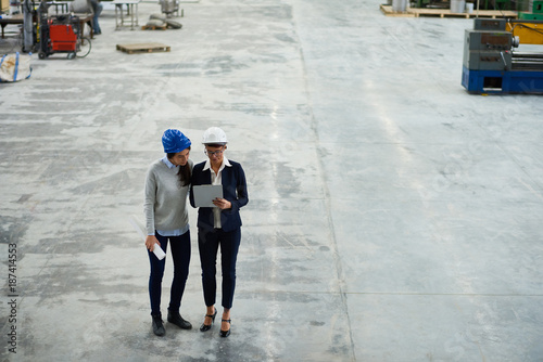 Wallpaper Mural Full length portrait of two modern female engineers wearing hardhats planning work writing on clipboard in workshop of modern factory, copy space Torontodigital.ca