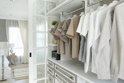 modern wooden wardrobe with clothes hanging on rail in walk in closet design interior photo