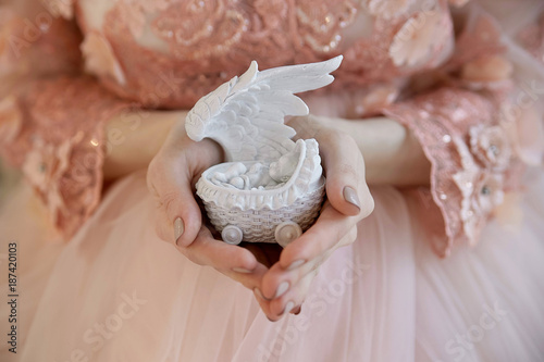 young pregnant girl in a pink dress is holding a statue of an angel. souvenir. close-up