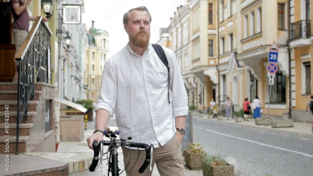 Slow motion video of stylish bearded man with his bucycle walking on narrow street of old town Slow motion video of stylish bearded man with his bucycle walking on narrow street of old town