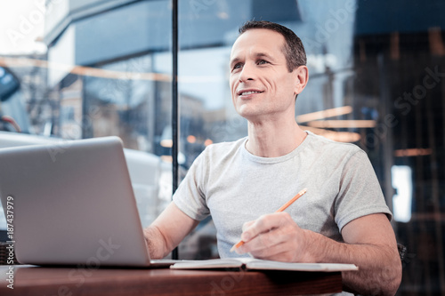 Have idea. Positive delighted man looking forward and holding pencil in left hand while sitting opposite his computer