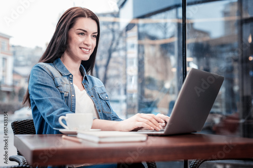 Online communication. Cheerful young woman expressing positivity while looking at screen of her laptop, sitting in semi position