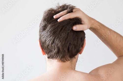Man touching his brown hair on the gray background. Cares about a healthy and clean hair. Beauty salon concept.