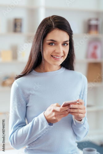 Online communication. Good looking happy elegant woman carrying phone while staring  at the camera and thinking about answer 