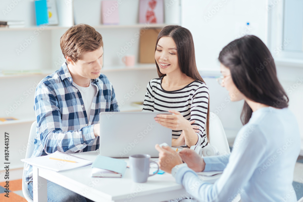 Fototapeta premium Team studying. Smart pleasant three students solving problem while looking down and posing on the light background 