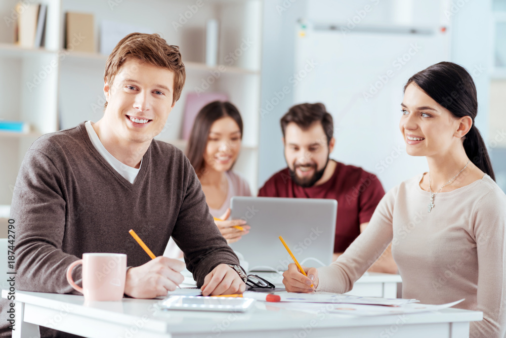 Love at work. Happy young two colleges holding pencils while working and woman admiring guy Love at work. Happy young two colleges holding pencils while working and woman admiring guy