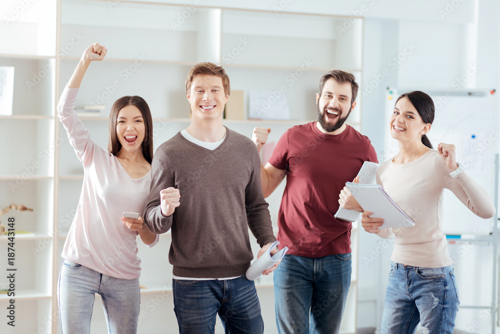 Good deal. Pretty merry four colleagues demonstrating happiness while standing and staring at the camera Good deal. Pretty merry four colleagues demonstrating happiness while standing and staring at the camera