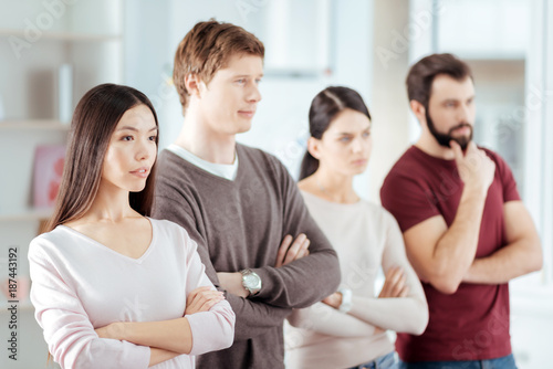  Good call. Focused earnest budding woman crossing arms while posing with three colleagues and looking straight 