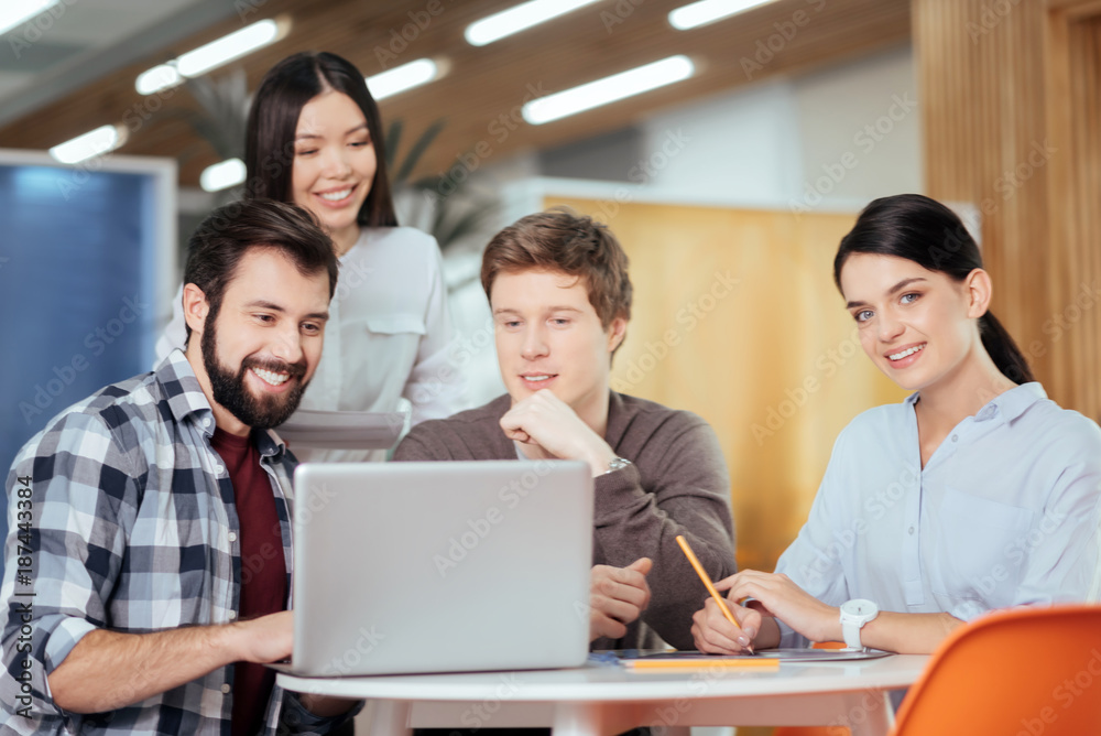 Positive changes. Attractive appealing four colleagues working on project while conducting research and laughing Positive changes. Attractive appealing four colleagues working on project while conducting research and laughing