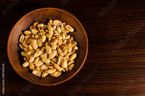 Peeled roasted peanuts in ceramic dish on wooden table. Top view