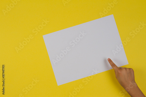 Kids hand finger pointing to white blank paper card on yellow background