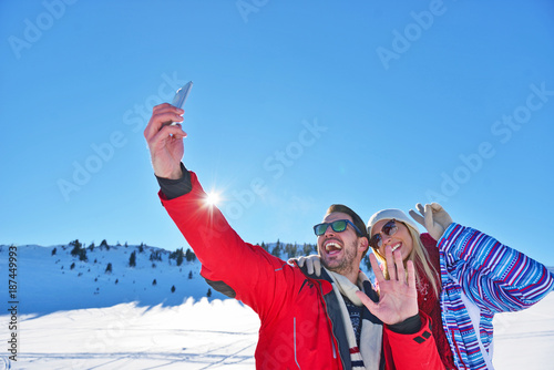 happy couple taking picture with smartphone selfie stick on over winter background