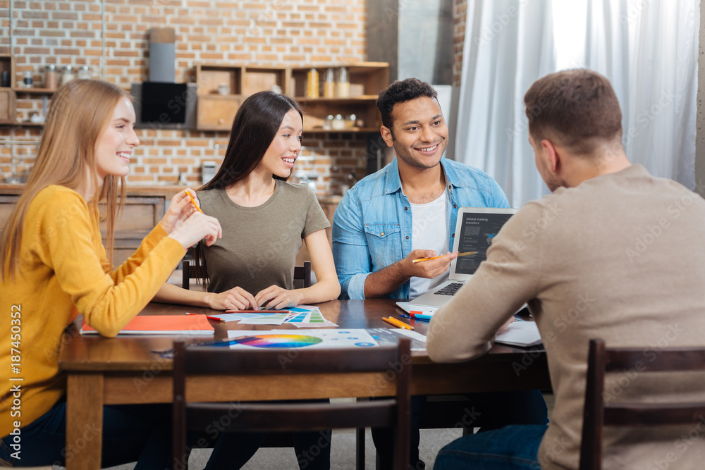Working together. Friendly cheerful young workers of the same company smiling while sitting together at the table and talking about the changes in their new interesting project