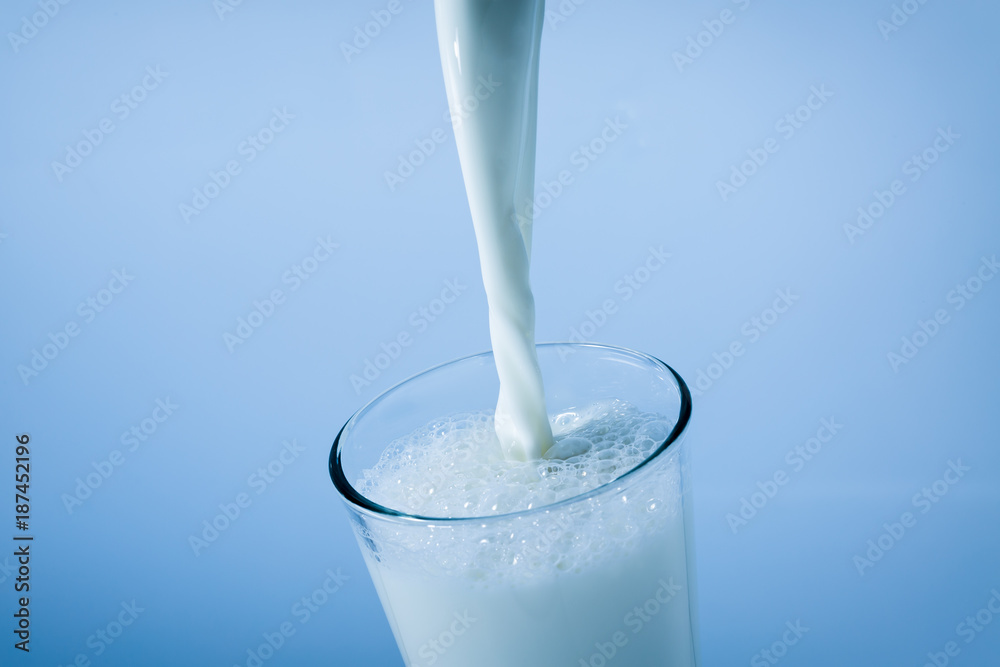 Pouring milk into a glass, splash on blue background Pouring milk into a glass, splash on blue background