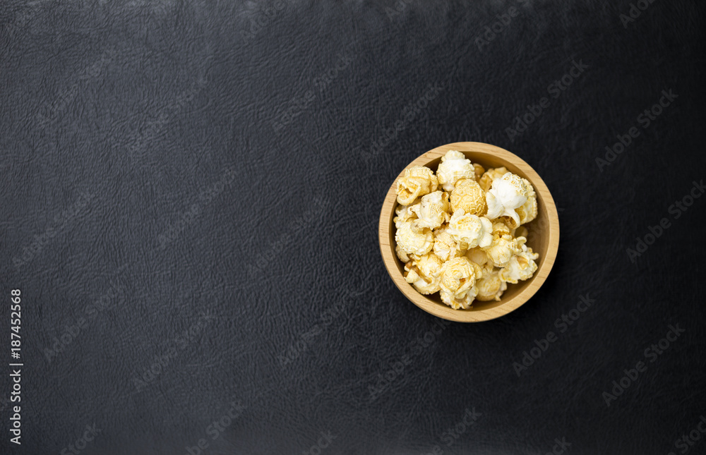 Salted popcorn in round wooden bowl on black leather texture background, movie night snack Salted popcorn in round wooden bowl on black leather texture background, movie night snack
