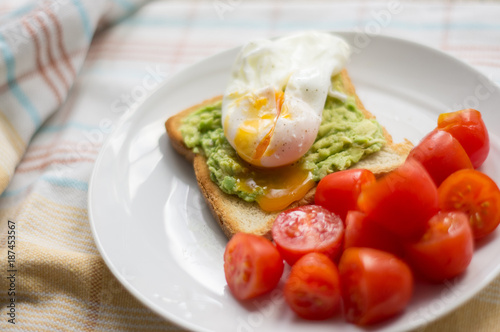 Perfect poached egg with avocado toast and fresh tomatoes on a white plate on a dish cloth