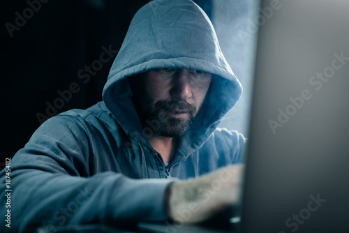 young guy hacker in a gray sweatshirt sits behind a laptop