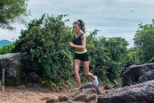 Fit athletic young woman running on dirty rocky path in mountains in summer.