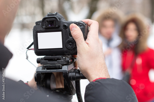 season, hobby, art work concept. close up of professional camera with blank screen in the arm of photographer on the background of two models that wear winter clothes