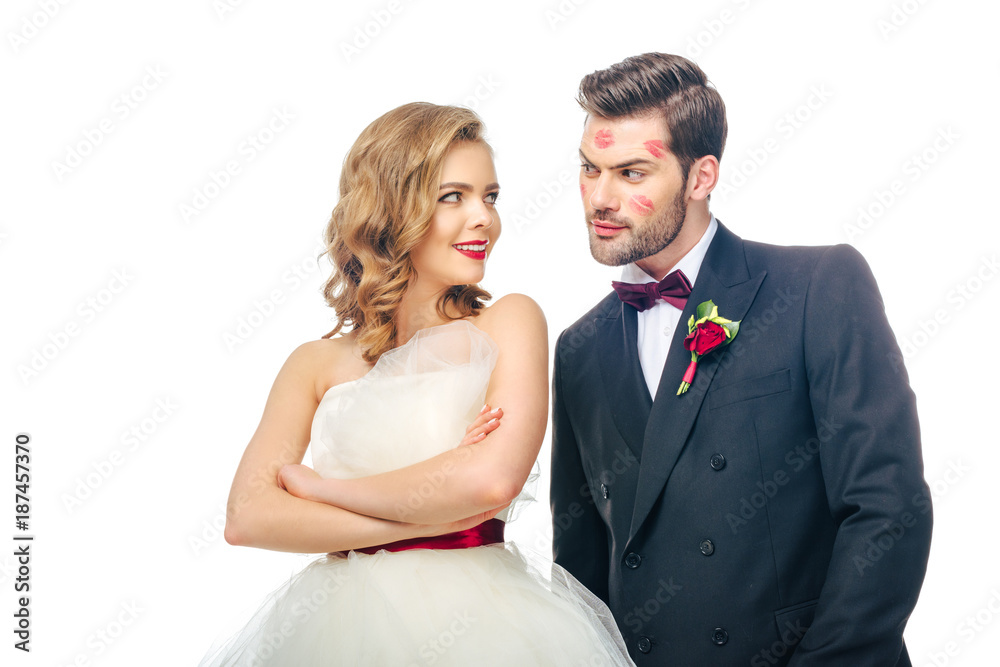 portrait of bride with arms crossed looking at groom with lipstick on face isolated on white portrait of bride with arms crossed looking at groom with lipstick on face isolated on white
