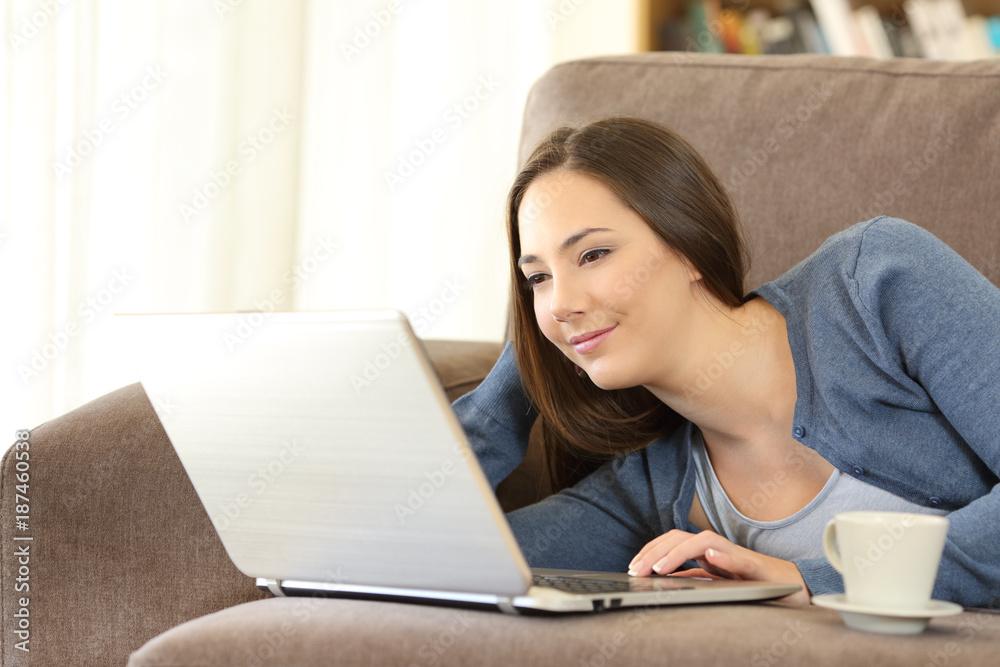 Woman using a laptop lying on a couch at home Woman using a laptop lying on a couch at home