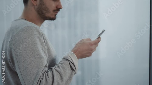 Portrait of young businessman talk on cellphone while stand by his office window in modern interior of skyscraper building, male entrepreneur having mobile phone conversation after important briefing photo