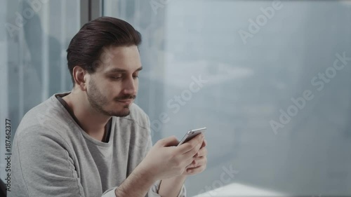 Portrait of young businessman talk on cellphone while stand by his office window in modern interior of skyscraper building, male entrepreneur having mobile phone conversation after important briefing photo