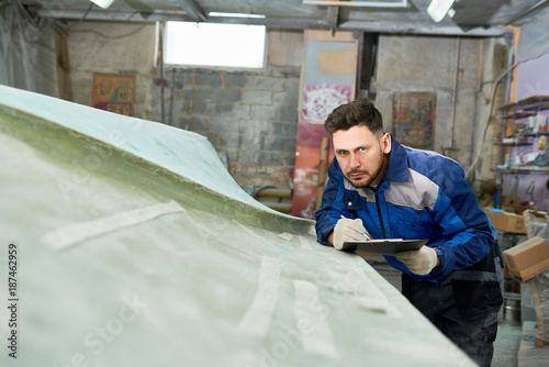 Fotografia Portrait of handsome worker making notes on clipboard while repairing boat in ya