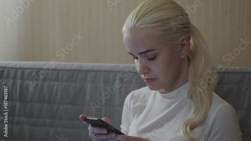 Girl using a smart phone voice recognition on line sitting on a sofa in the living room at home with a warm light blonde model student photo