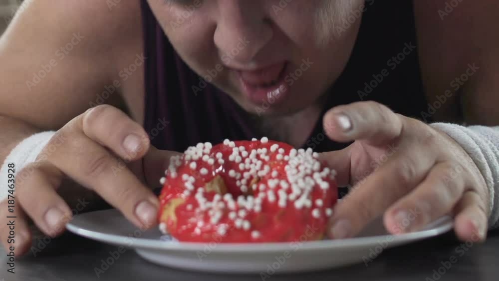 Overweight adult man lying on the floor and chewing donut with appetite, closeup Overweight adult man lying on the floor and chewing donut with appetite, closeup
