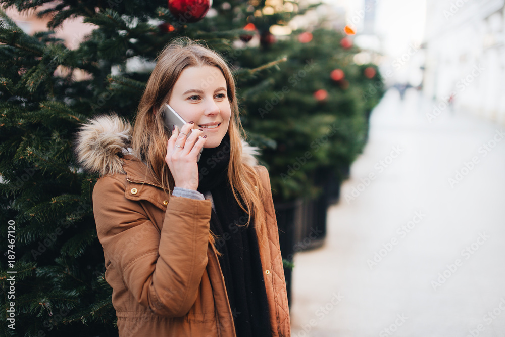 Happy girl talk on her phone and look around with smile impression on her face. Winter time with tree on the street. Happy girl talk on her phone and look around with smile impression on her face. Winter time with tree on the street.