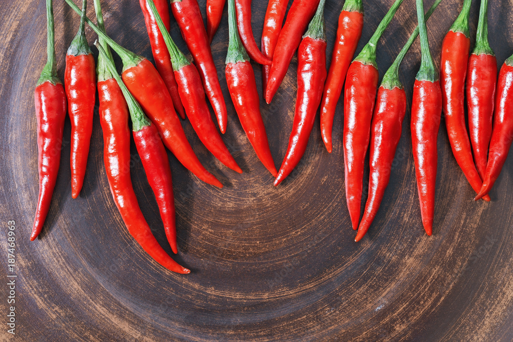 Food background with red hot chili peppers with free space for text. Fresh spicy peppers on brown clay plate. Top view. Food background with red hot chili peppers with free space for text. Fresh spicy peppers on brown clay plate. Top view.