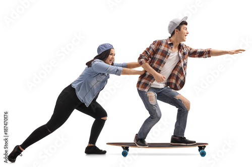 Teenage girl pushing a teenage boy on a longboard