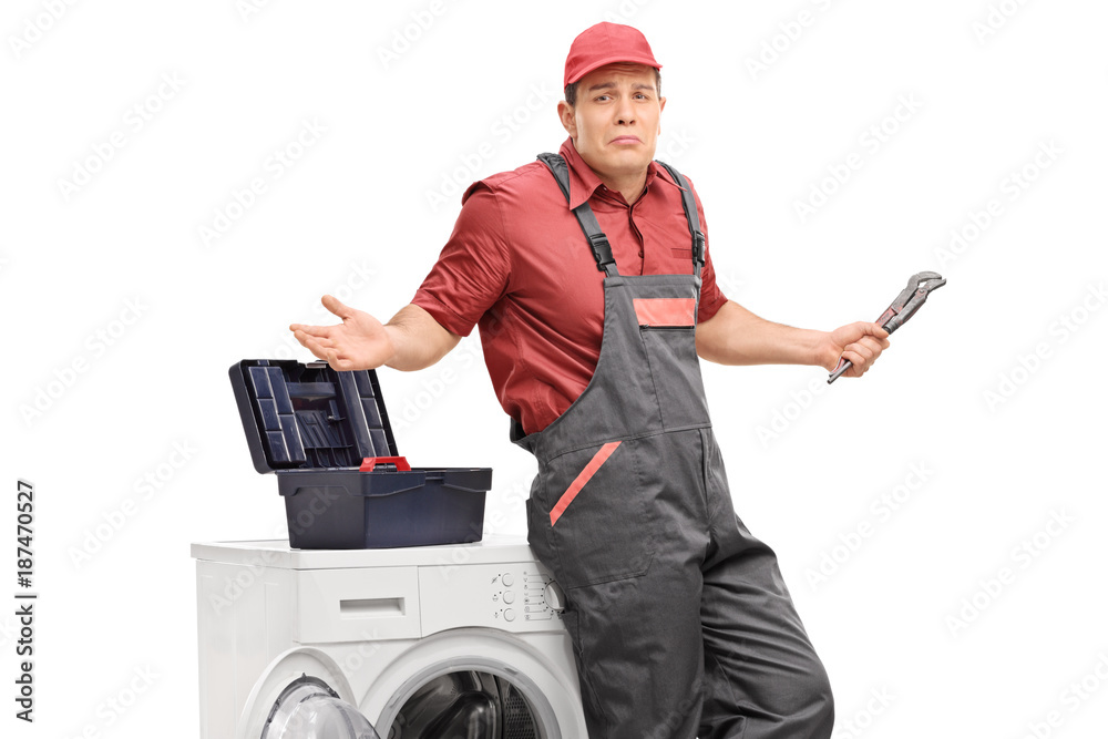 Uncertain repairman with a wrench leaning against a washing machine Uncertain repairman with a wrench leaning against a washing machine