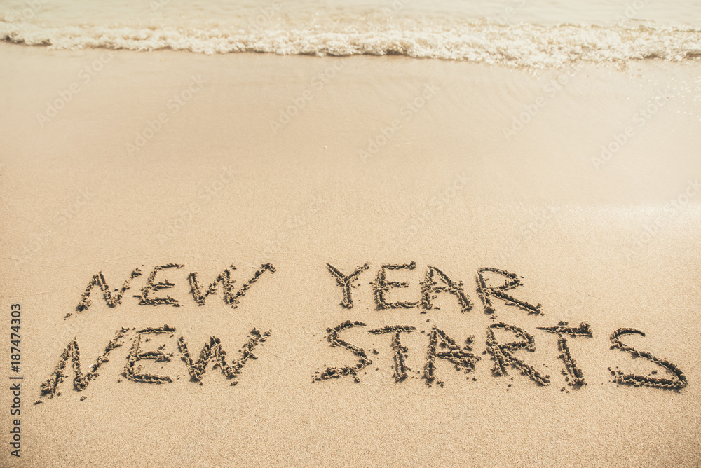 Fototapeta premium New Year New Starts text written on the sand