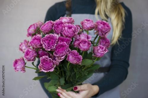 The big bouquet of pink roses in female hands on gray background