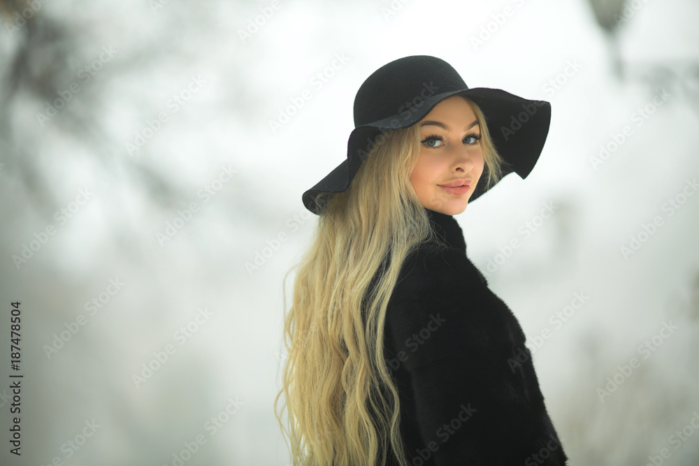 beautiful young girl in fur coat and hat walking in the park in winter weather beautiful young girl in fur coat and hat walking in the park in winter weather