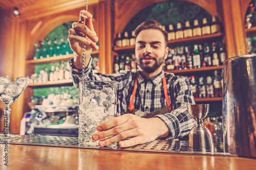 Barman making an alcoholic cocktail at the bar counter on the bar background