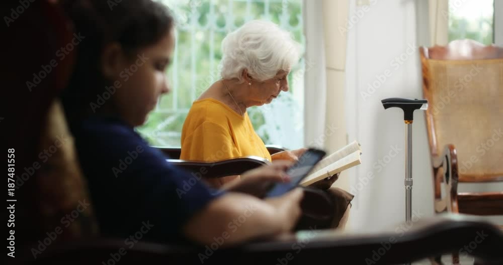 Granddaughter Using Mobile Phone And Grandma Reading Book Granddaughter Using Mobile Phone And Grandma Reading Book