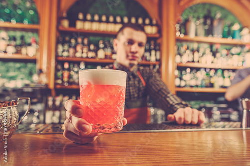 Barman offering an alcoholic cocktail at the bar counter on the bar background