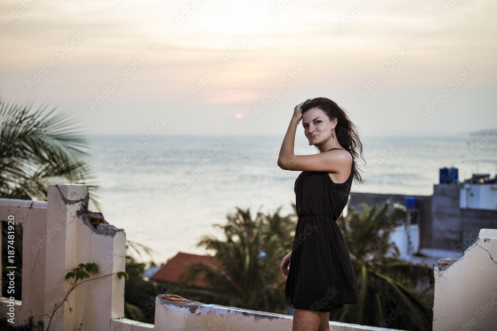 Obraz premium Beautiful woman model fashionable and sexy on the balcony overlooking the sea, palm trees and sunset